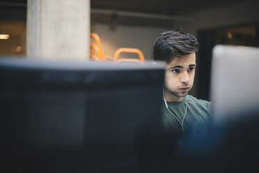 Male computer programmer puffing cheeks while using desktop PC in office - MASF01632