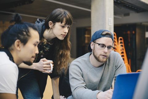 Male and female computer programmers using laptop at desk in office stock photo