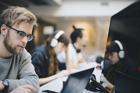 Männlicher Programmierer arbeitet am Computer mit Kollegen am Schreibtisch im Büro - MASF01639