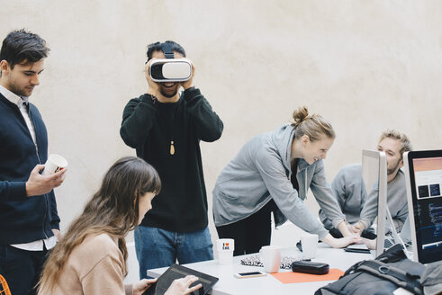 Männlicher Computerprogrammierer, der eine VR-Brille benutzt, während seine Kollegen im Büro arbeiten - MASF01640