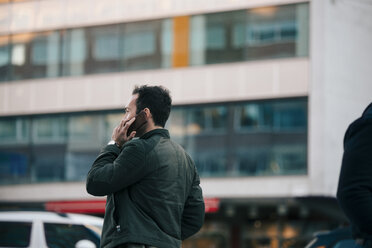 Man talking on mobile phone while standing against building in city - MASF01658