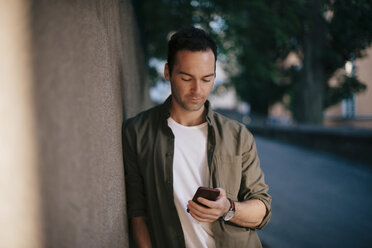 Man using mobile phone while leaning on wall - MASF01659