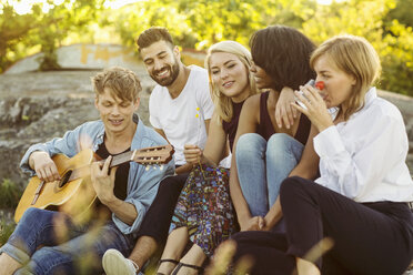 Man playing guitar while friends enjoying during summer - MASF01667