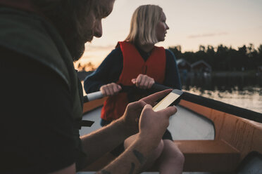 Mann benutzt Mobiltelefon, während Frau auf dem See rudert - MASF01672