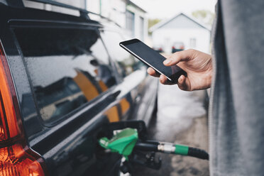 Man using mobile phone while refueling car at gas station - MASF01675