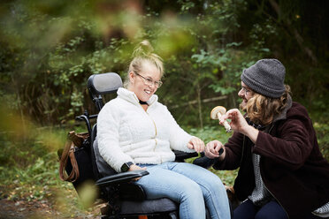 Männlicher Hausmeister zeigt einer behinderten Frau im Rollstuhl im Wald einen Pilz - MASF01679