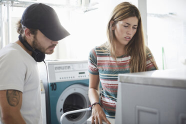 Mann hilft einer Freundin bei der Benutzung der Waschmaschine in einem Waschsalon an einem sonnigen Tag - MASF01681