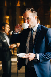 Reifer Geschäftsmann trinkt Kaffee, während er vor der Spiegelung eines männlichen Kollegen auf einem Glas steht - MASF01691