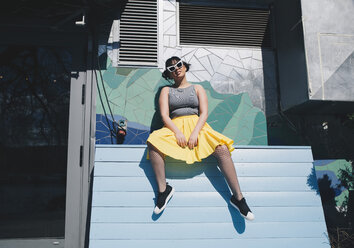 Low angle portrait of young woman sitting on bench against mosaic wall - MASF01714