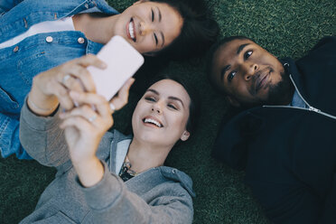 High angle view of smiling woman taking selfie with friends while lying on grass - MASF01733