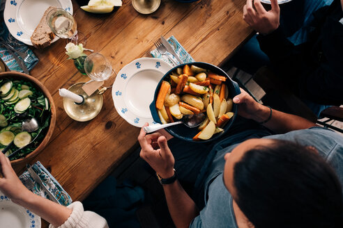 Hohe Winkel Ansicht des Mannes hält Utensil von Kartoffeln und Karotten beim Sitzen mit Freunden - MASF01744