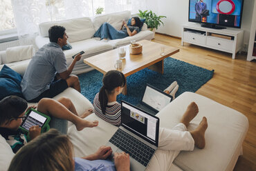 Blick von oben auf die Familie bei der Nutzung von Technologien, während sie sich im heimischen Wohnzimmer entspannt - MASF01765