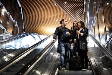 Niedriger Blickwinkel auf Freunde mit Gepäck, die sich auf einer Rolltreppe in einer U-Bahn-Station unterhalten - MASF01769