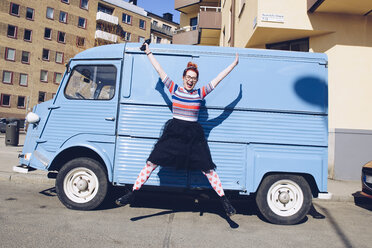 Junge Frau springt in voller Länge gegen einen blauen Mini-Van auf einer Straße in der Stadt - MASF01777