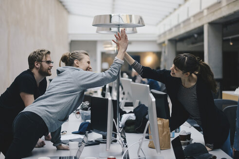 Glückliche weibliche Computerprogrammierer, die sich über dem Schreibtisch im Büro die Hände reichen - MASF01779