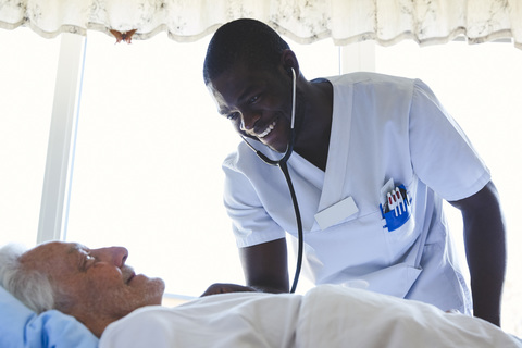 Glücklicher Krankenpfleger, der einen älteren Mann mit einem Stethoskop in einer Krankenstation untersucht, lizenzfreies Stockfoto
