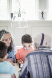 Großeltern beobachten einen Jungen, der zu Hause ein digitales Tablet benutzt - MASF01796