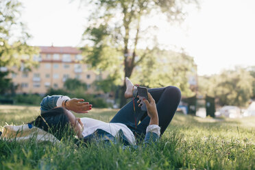 Teenager-Mädchen in voller Länge, das sein Smartphone benutzt, während es im Gras liegt - MASF01803