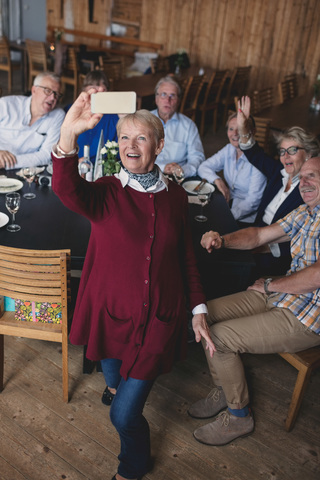Glückliche ältere Frau, die ein Selfie mit Freunden mit dem Handy im Restaurant macht, lizenzfreies Stockfoto