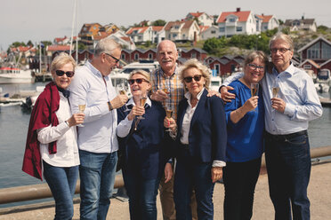 Glückliche ältere männliche und weibliche Freunde genießen Champagner auf Pier im Urlaub - MASF01827