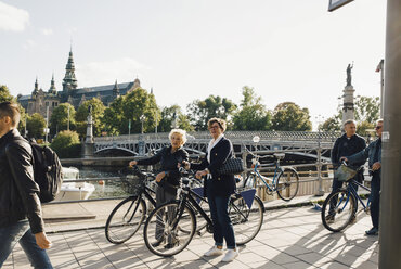 Volle Länge von älteren Frauen mit Fahrrädern, die wegschauen, während sie auf dem Bürgersteig in der Stadt stehen - MASF01836