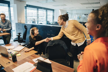 Happy colleagues shaking hands in office - MASF01840