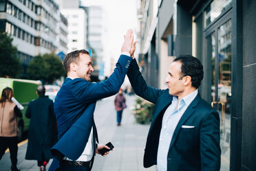 Happy mature male business coworkers giving high-five while standing on sidewalk in city - MASF01841