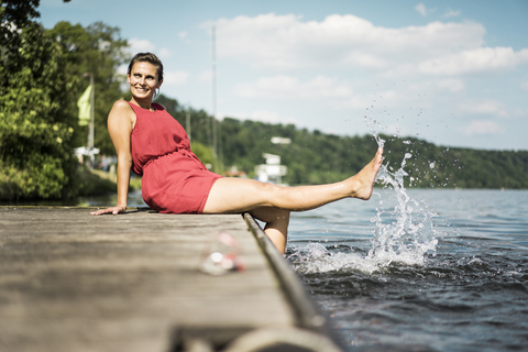 Glückliche Frau sitzt auf einem Steg an einem See, lizenzfreies Stockfoto