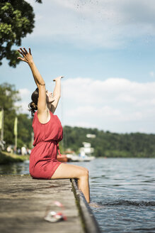 Glückliche Frau sitzt auf einem Steg an einem See - JOSF02164