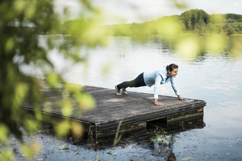 Frau macht Liegestütze auf einem Steg an einem See, lizenzfreies Stockfoto