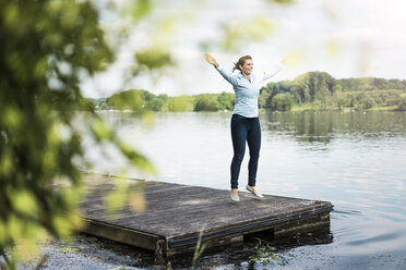 Woman doing a jumping jack on jetty at a lake - JOSF02172