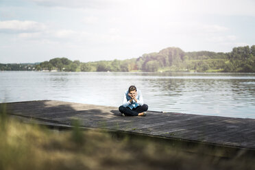 Entspannte Frau sitzt auf einem Steg am See - JOSF02173