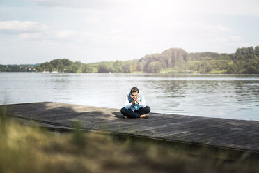 Relaxed woman sitting on jetty at a lake - JOSF02173