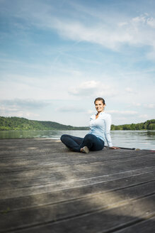 Lächelnde Frau auf einem Steg an einem See sitzend - JOSF02174
