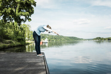Woman on jetty wearing VR glasses pretending to dive into a lake - JOSF02175