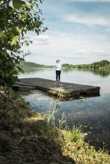 Frau steht auf einem Steg an einem See und trägt eine VR-Brille - JOSF02176