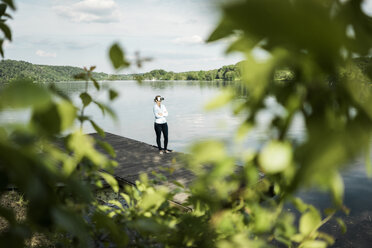 Woman standing on jetty at a lake wearing VR glasses - JOSF02177