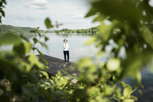 Frau steht auf einem Steg an einem See und trägt eine VR-Brille - JOSF02177