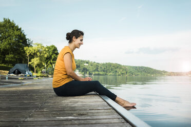 Happy woman sitting on jetty at a lake - JOSF02179