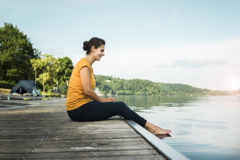Glückliche Frau sitzt auf einem Steg an einem See - JOSF02179