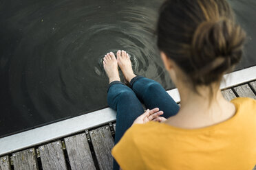 Woman sitting on jetty at a lake with feet in water - JOSF02180