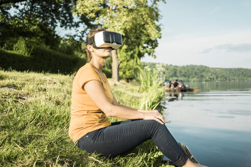 Frau sitzt an einem See und trägt eine VR-Brille - JOSF02182