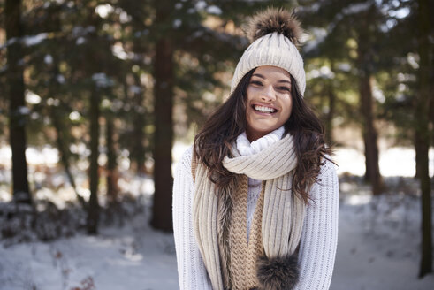 Porträt einer lachenden jungen Frau in Strickwaren im Winterwald - ABIF00279