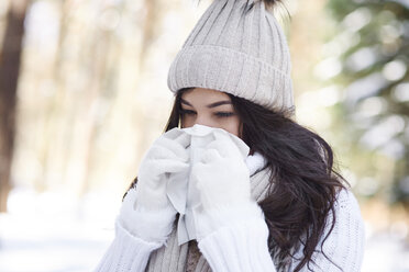 Young woman blowing nose in winter - ABIF00284