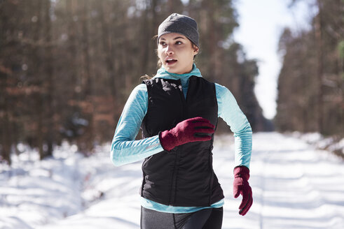 Portrait of young woman jogging in winter forest - ABIF00292