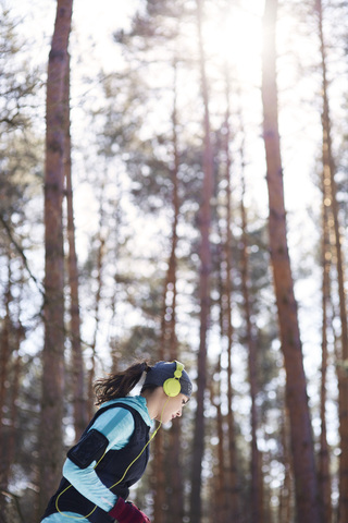 Young woman with headphones jogging in winter forest stock photo