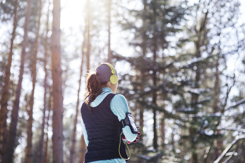 Rückenansicht einer jungen Joggerin mit Kopfhörern im Wald, die eine Pause macht, lizenzfreies Stockfoto