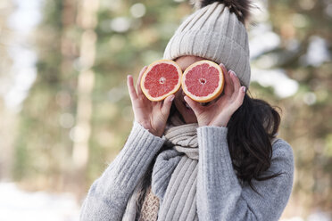 Lachende junge Frau in Strickwaren, die ihre Augen mit Grapefruithälften bedeckt - ABIF00299