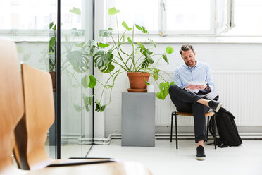 Confident businessman holding paper while sitting on chair at creative office - MASF01857