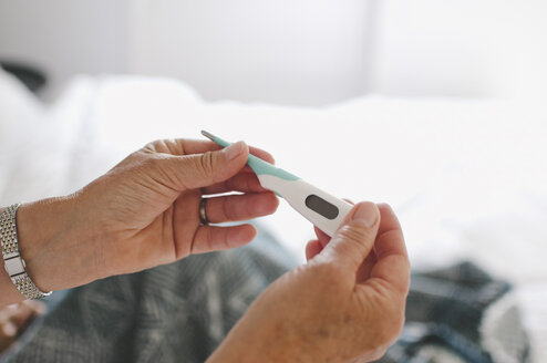 Ausgeschnittenes Bild einer älteren Frau, die ein Thermometer zu Hause untersucht - MASF01860